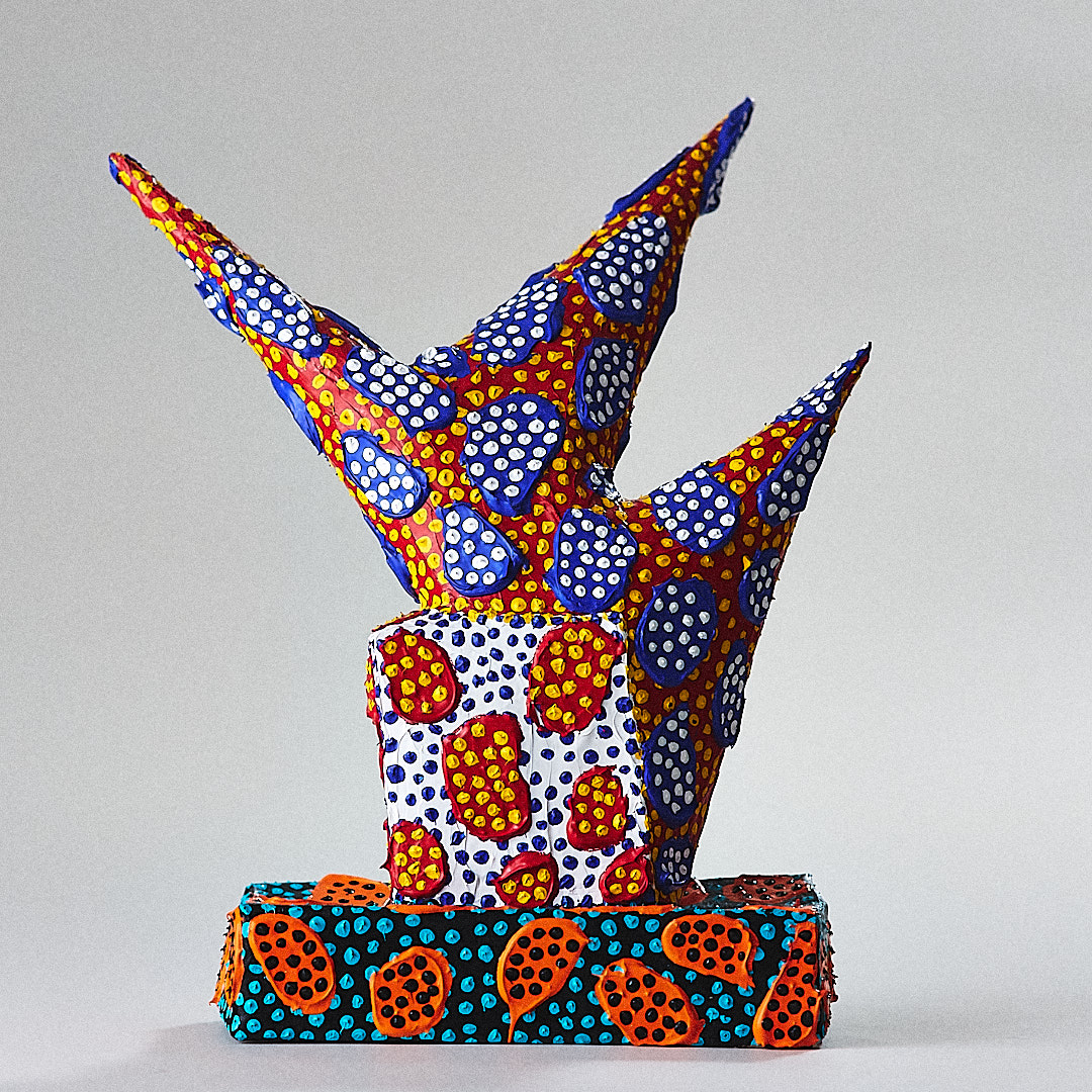 A horned sculpture patterned in red, blue, yellow and white stands on a rectangular base.